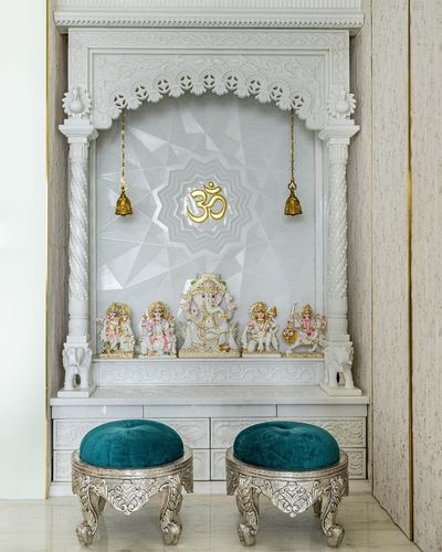 White marble pooja mandir with carved arch, deity idols, and teal velvet stools