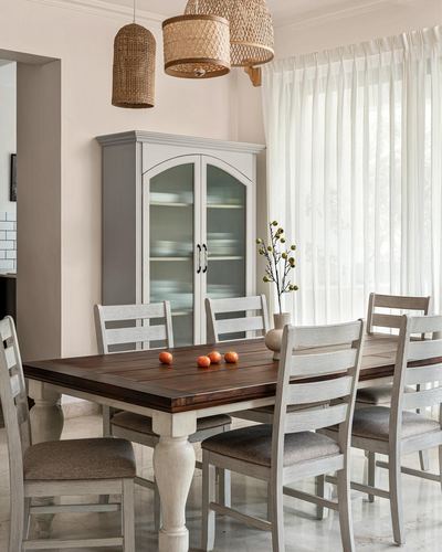 Dining room with wooden farmhouse table, upholstered chairs, glass cabinet and woven pendant lights