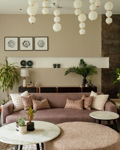 Living room with mauve velvet sofa, globe pendant cluster, and floating display shelf against beige wall
