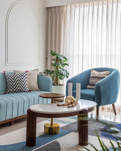 Blue channel-tufted sofa and armchair around a ribbed marble-top coffee table by sheer curtained windows