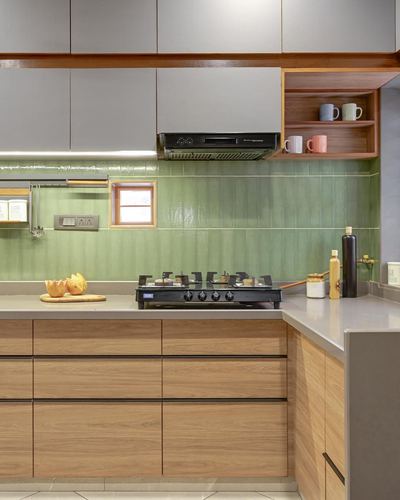 L-shaped kitchen with green ribbed tile backsplash, wood cabinetry, and open shelf with colorful mugs