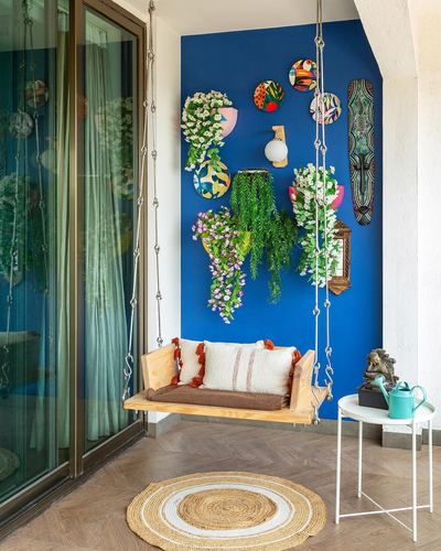 Wooden hanging swing on balcony against cobalt blue wall with plates and hanging plants