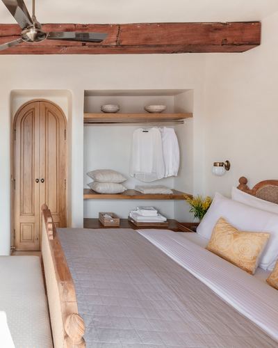 Rustic bedroom with arched wooden door, open shelving niche, and wood-beamed ceiling in soft neutral tones