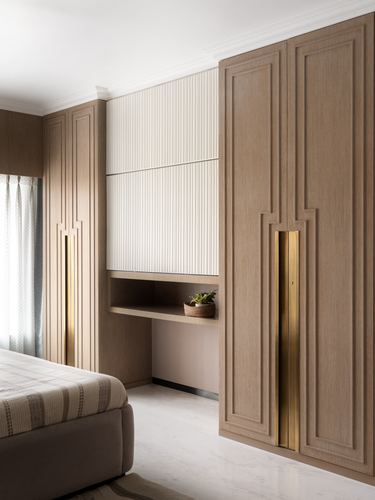 Beige wardrobe wall with fluted panel niche, brass handles, and built-in desk in bedroom