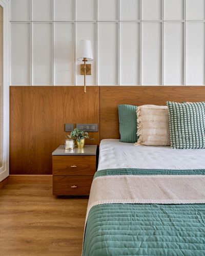 Bedroom corner with wood headboard wall, brass sconce, nightstand, and green-cream bedding