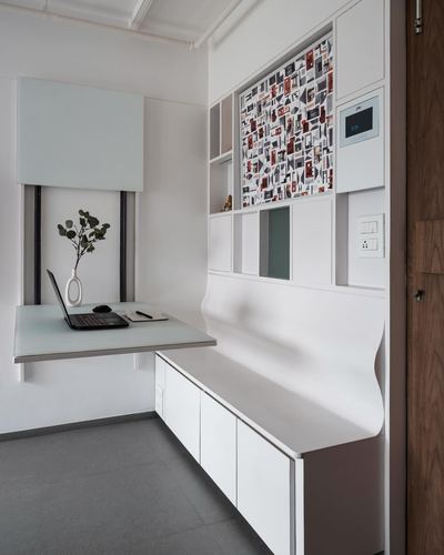 White fold-down desk with laptop beside a curved built-in counter and shelving unit