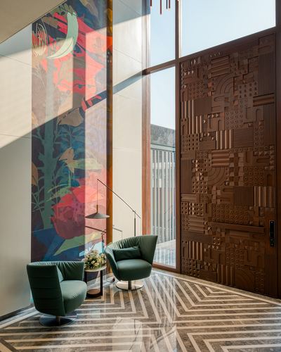 Double-height entrance foyer with carved wooden door, green swivel chairs, and geometric marble floor