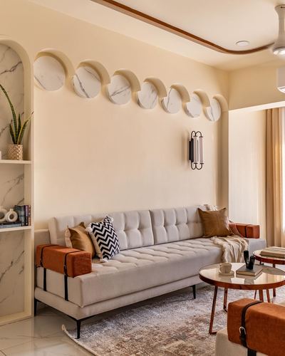 Cream living room with tufted sofa, terracotta bolsters, and overlapping marble discs on wall