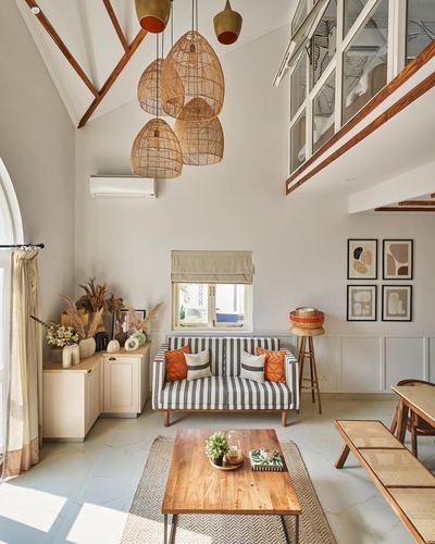 Double-height living room with rattan pendant cluster, striped sofa, and wooden coffee table under skylight loft
