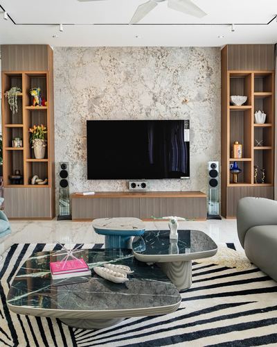 Living room with textured stone wall, wood shelving, TV, and layered marble coffee tables on striped rug