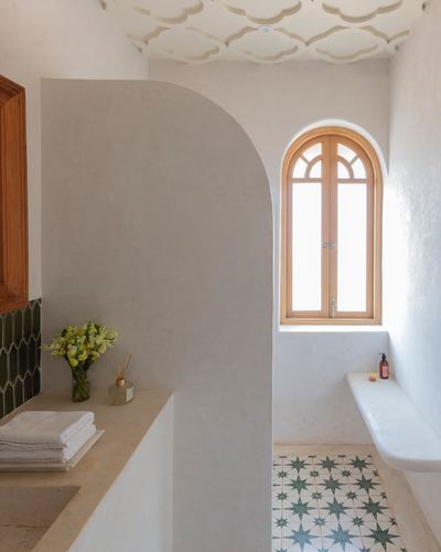 Bathroom with arched wooden window, curved plaster wall, and star-patterned green tile floor