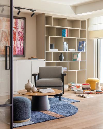 Living room corner with grid bookshelf, houndstooth armchair, round wood table on blue rug.