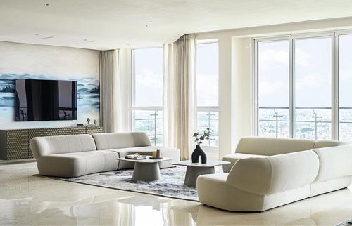 Curved living room with two beige sofas, round coffee tables and floor-to-ceiling windows overlooking the city