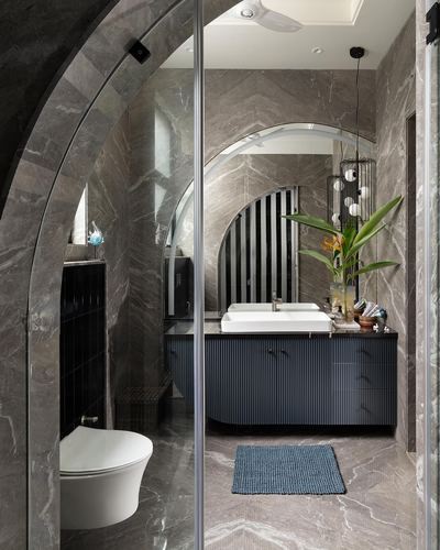 Bathroom with arched glass shower, veined stone walls, dark fluted vanity and pendant light