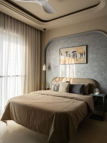 Beige and grey bedroom with arched textured headboard wall, upholstered bed, and sheer curtained window in soft daylight