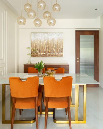 Dining room with orange velvet chairs, glass-brass table, and globe pendant cluster