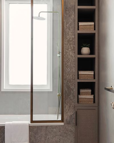 Bathroom corner with stone tile, glass shower screen, brass fixtures and open wood shelving with baskets
