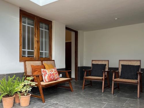 Covered veranda with cane-backed wooden bench and chairs, terracotta cushions, potted plants, stone flooring