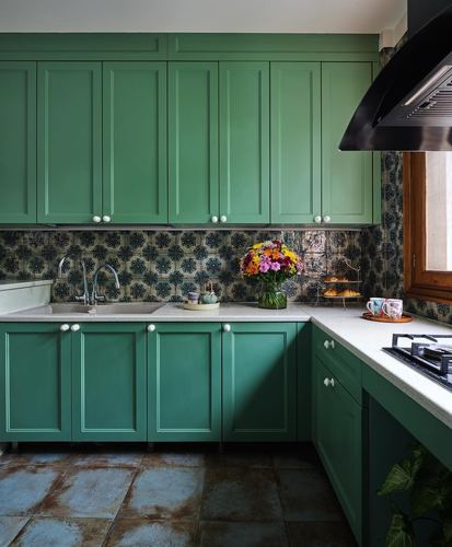 Green cabinetry kitchen with patterned tile backsplash, terracotta floor, and flowers on the counter