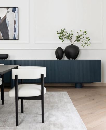 Dining nook with black chair, fluted navy sideboard, and black ceramic vases against white paneled wall