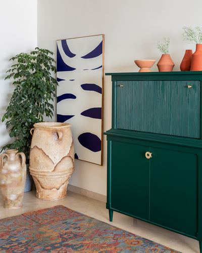 Corner vignette with terracotta urns, blue abstract art, and a green fluted cabinet topped with terracotta vases