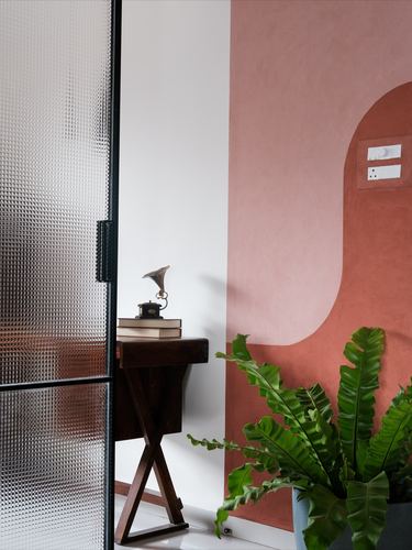 Terracotta plastered wall with arched niche beside reeded glass door and wooden stool with plant