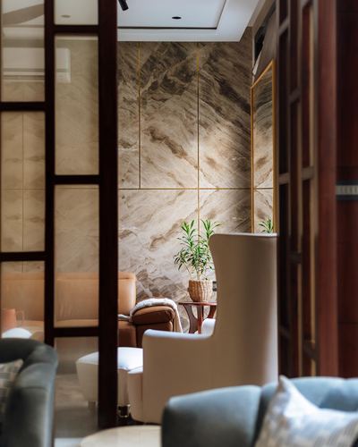 Lounge seen through timber screen with book-matched stone wall, wing chairs, and potted plant