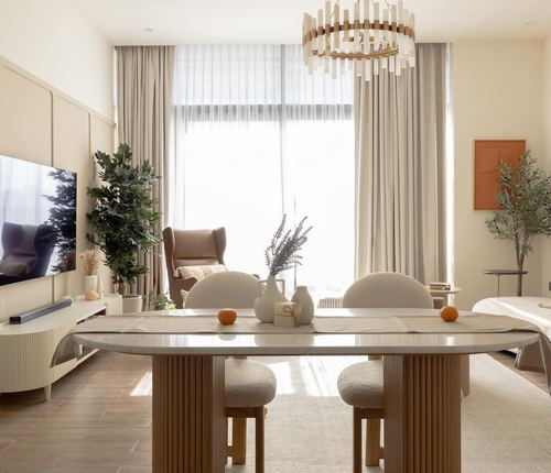 Sunlit dining and living area with oval table, boucle stools, wingback chair and sculptural wood chandelier
