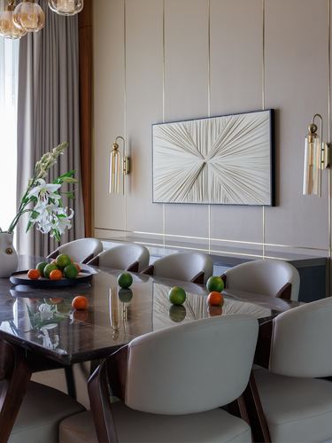 Dining table set with fruit under sconces and a textured wall panel in a beige dining room
