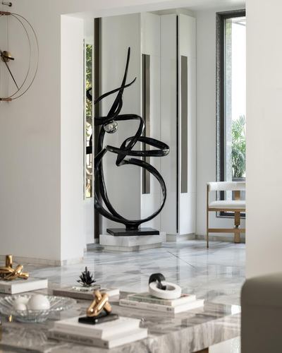 Black abstract sculpture on marble base in mirrored foyer alcove with marble floor and coffee table