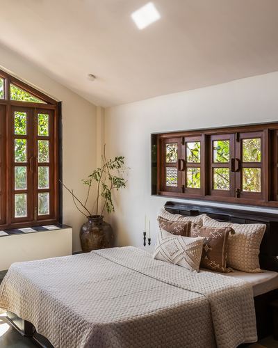 Bedroom with dark wood-framed arched windows, quilted bed, and terracotta pot in natural light