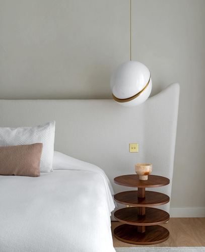 Cream boucle headboard beside a tiered wood side table under a round pendant light