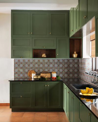 Olive green kitchen with patterned tile backsplash, black countertop, and brass vessels displayed on open shelf