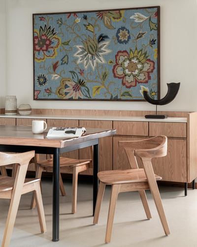 Dining area with wooden chairs, live-edge table, and floral tapestry above a wood sideboard