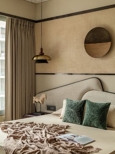 Bedroom corner with beige headboard, brass pendant light, and green patterned cushions against textured tan wall
