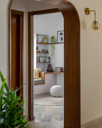 View through a curved wooden archway into a small study nook with shelves and window seat