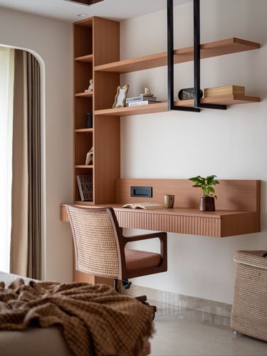 Wooden wall-mounted desk with cane chair and floating shelves in a minimalist study nook