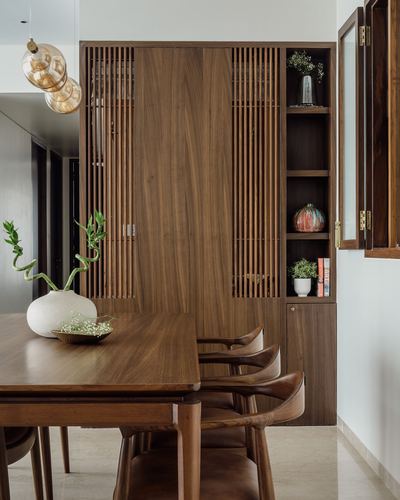 Wooden dining table with carved chairs beside a fluted wood cabinet and open shelving display