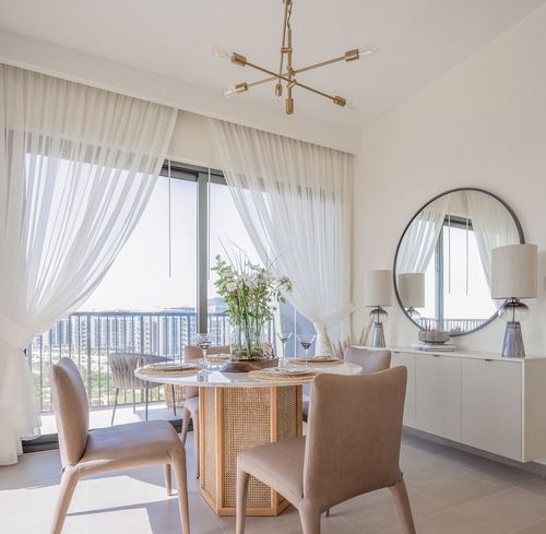 Dining table with cane base and marble top beneath brass chandelier, sheer curtains and city view
