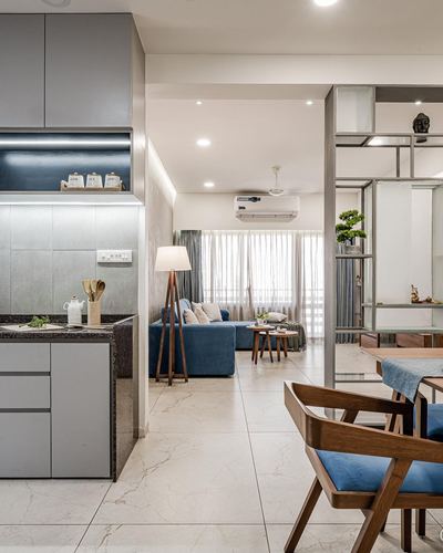 Open-plan apartment interior showing grey kitchen counter, blue sofa living room and wood dining chairs beyond