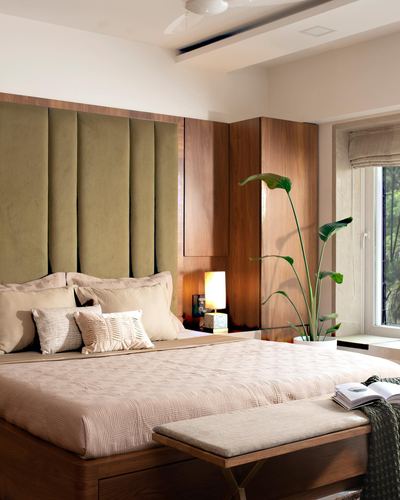 Bedroom with olive velvet channel headboard, walnut panelling, and large leafy plant by window
