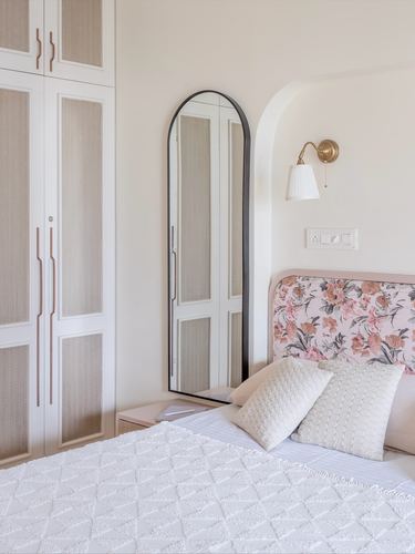 Bedroom corner with arched mirror, cane wardrobe, floral pink headboard and brass wall sconce