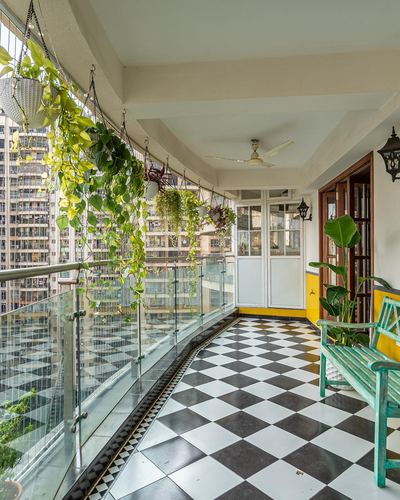 Long balcony with checkerboard tile floor, hanging plants, glass railing overlooking city skyline