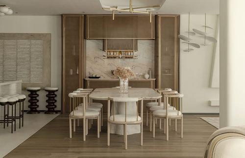 Dining room with oval marble table, upholstered chairs, and a marble-clad bar niche framed in brass