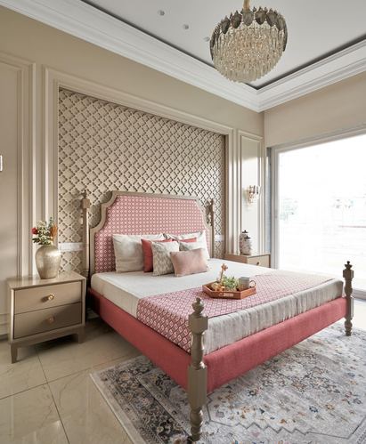 Bedroom with pink upholstered four-poster bed against quilted beige wall panel and crystal chandelier
