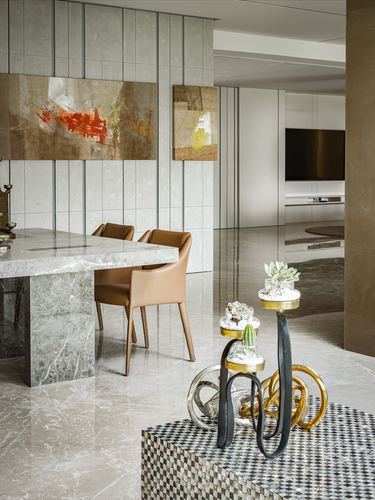 Marble dining table with tan leather chairs beside sculptural brass side tables and abstract art