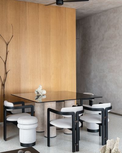 Dining area with glass table on stone base, black-framed boucle chairs, wood wall panel