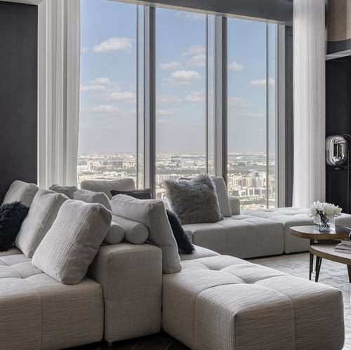 Grey tufted sectional sofa facing floor-to-ceiling windows overlooking a high-rise city skyline