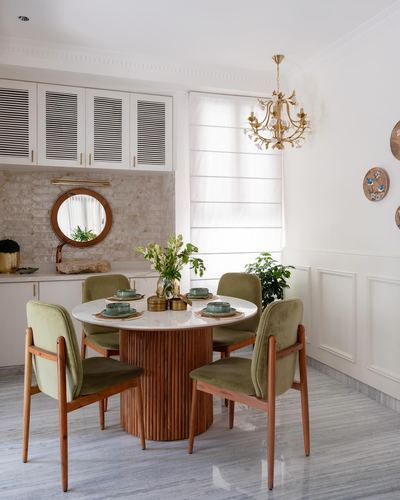 Round marble dining table with fluted wood base and olive velvet chairs under brass chandelier