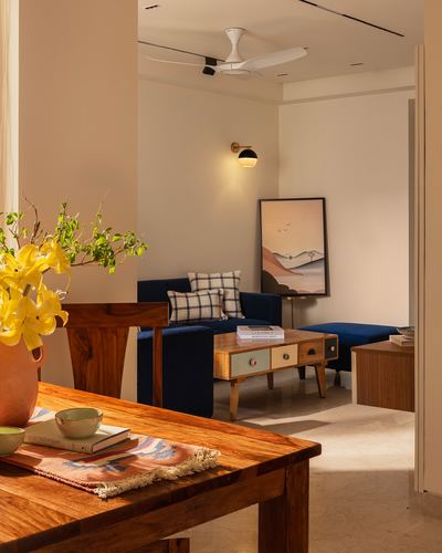 Living room with navy velvet sofa, wooden coffee table, and leaning artwork, seen past a dining table